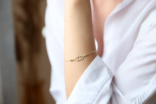 A woman wearing a dainty gold bracelet with a lotus flower design on her wrist.