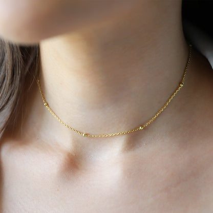 A woman wearing a gold beaded chain necklace with a satin finish.