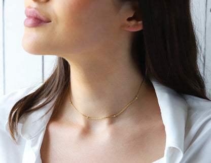 A woman wearing a gold beaded chain necklace with a satin finish.