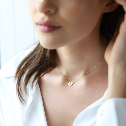 Woman wearing a gold necklace with a heart pendant against a blurred background