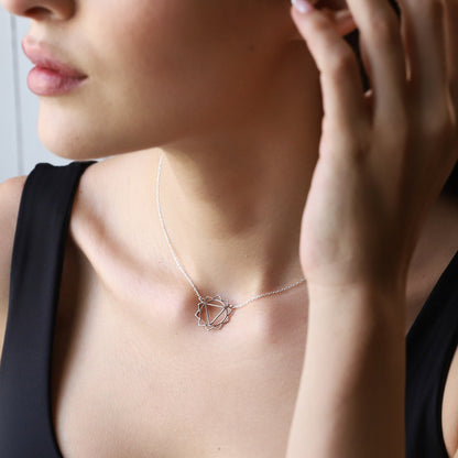 A person wearing a silver chakra necklace with a geometric design around the neck.