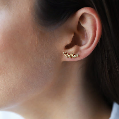 A close-up image of a person wearing a gold-toned stud earring with a custom name on it.