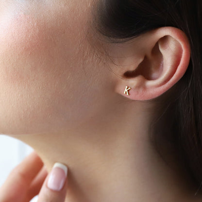 A close-up image of a person's ear wearing a small gold stud earring with the number 'K'.