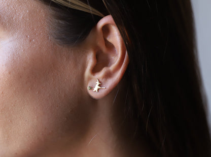 A close-up image of a person's ear wearing a small gold stud earring with a witch design