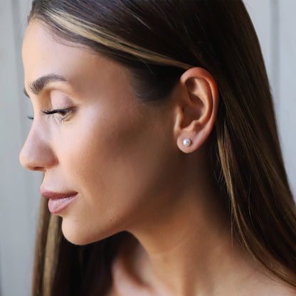 Close-up of a woman wearing pearl earrings with a neutral background