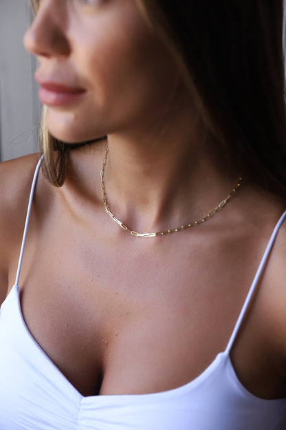 A close-up image of a person wearing a gold-filled loop chain necklace with a delicate and dainty design.