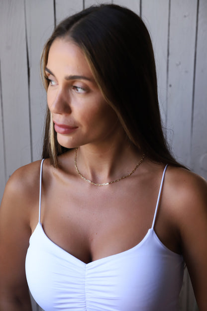 A close-up image of a person wearing a gold-filled loop chain necklace with a delicate and dainty design.