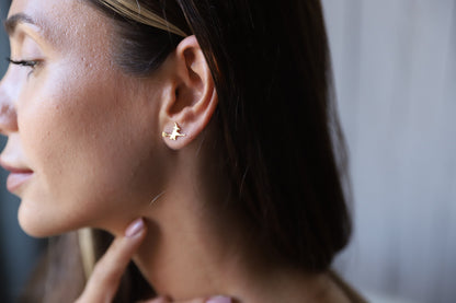A close-up image of a person's ear wearing a small gold stud earring with a witch design