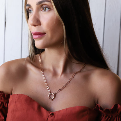 A person wearing a gold link chain necklace with a paperclip-shaped pendant and Sailor Lock.