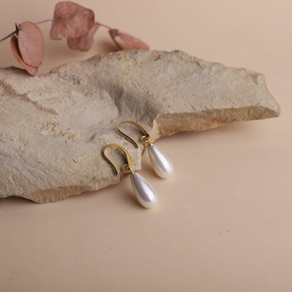 Pearl earrings with gold hooks on a stone surface
