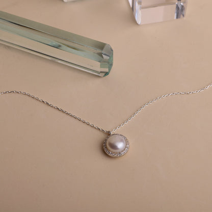 A woman wearing necklace with a pearl drop pendant, gold chain, and round pearl jewelry.