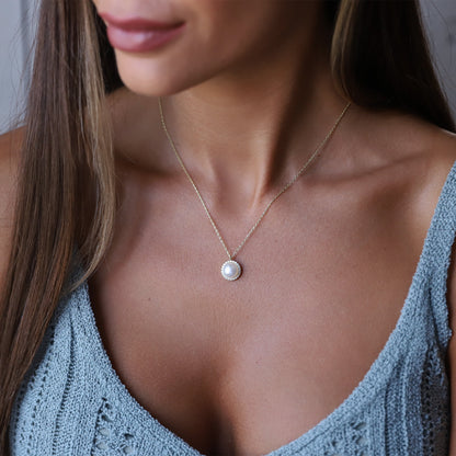 A woman wearing a dainty pearl necklace with a pearl drop pendant, gold chain, and round pearl jewelry.