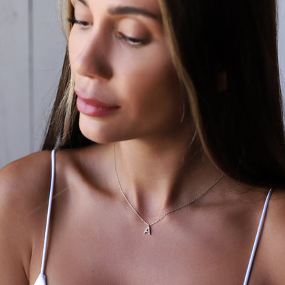 A close-up image of a woman wearing a custom dainty dangle pendant necklace with a pave initial design, in silver color.