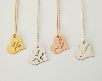 Four heart-shaped necklaces with engraved messages on a light gray background