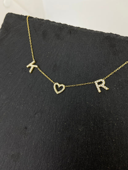 A close-up image of a dainty two-initial pave necklace with a heart-shaped charm.