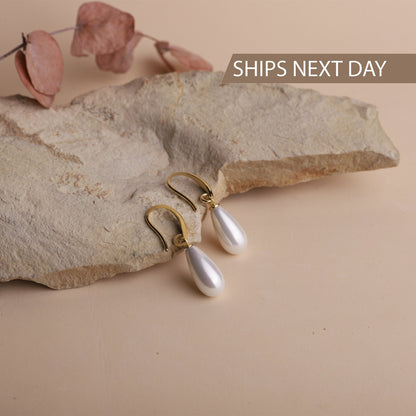 Pearl earrings with gold hooks on a stone surface
