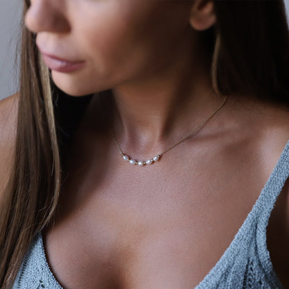 A person wearing a small freshwater beaded pearl necklace in gold tone.
