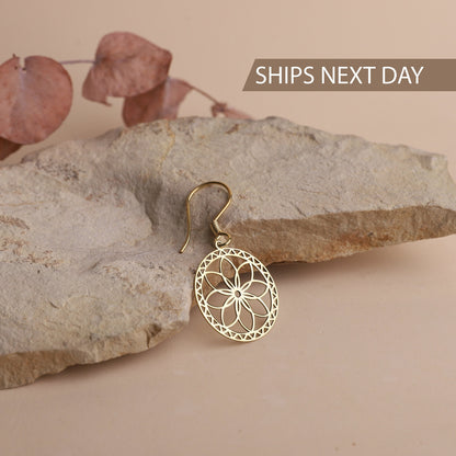 A gold-colored mandala dangle earring displayed on a rock, with the text 'SHIPS NEXT DAY' indicating the earrings are ready to ship.