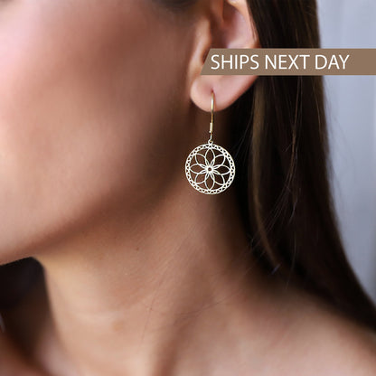 A woman wearing dangle gold mandala earrings with a geometric design, her earrings are gold and the rest of the earrings are silver.
