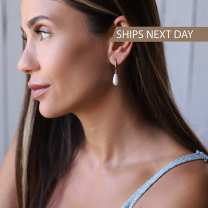 A woman wearing drop pearl earrings with the text 'SHIPS NEXT DAY' on the screen.