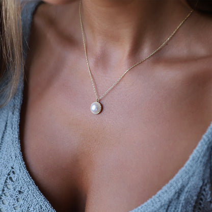 A woman wearing a dainty pearl necklace with a pearl drop pendant, gold chain, and round pearl jewelry.