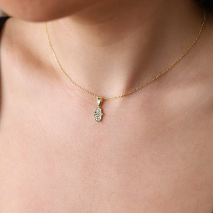 A person wearing a gold-colored Hamsa Charm Necklace with a Hand of Fatima design and pave CZ diamonds.