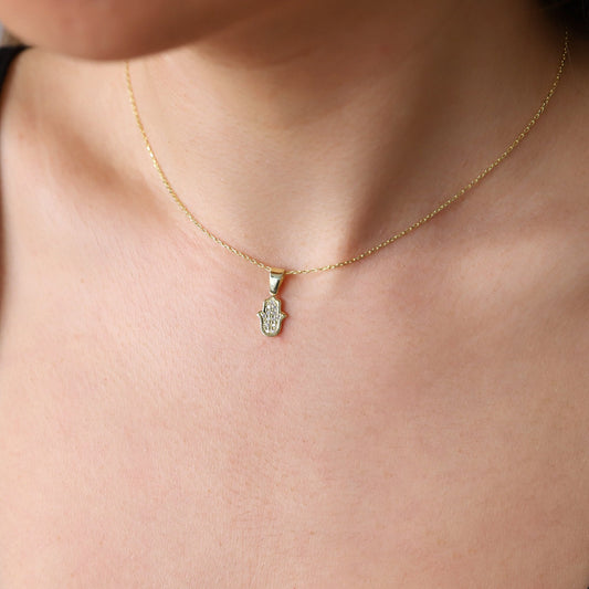 A person wearing a gold-colored Hamsa Charm Necklace with a Hand of Fatima design and pave CZ diamonds.