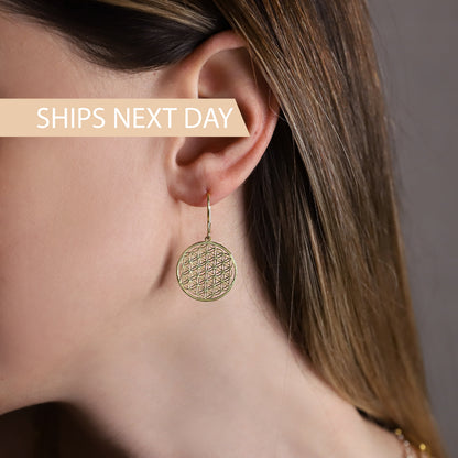 A women wearing a gold earrings featuring the Flower of Life pattern.