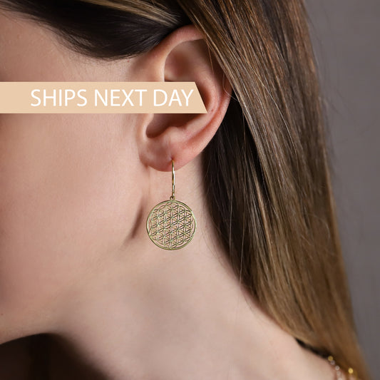 A women wearing a gold earrings featuring the Flower of Life pattern.