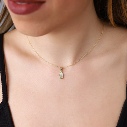 A person wearing a gold-colored Hamsa Charm Necklace with a Hand of Fatima design and pave CZ diamonds.