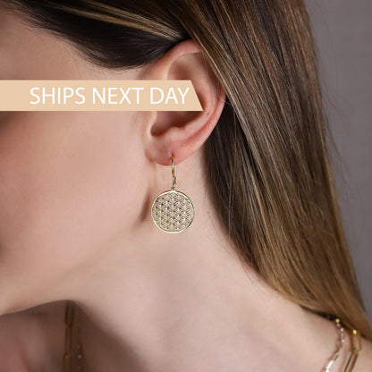 Close up picture of A women wearing a gold earrings featuring the Flower of Life pattern.
