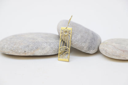 A person wearing a dangle earrings with a sun and ocean wave design.