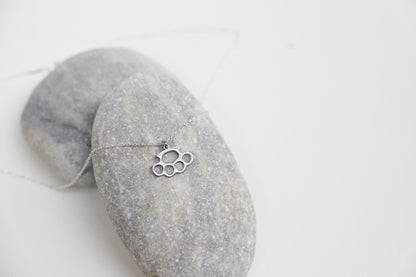 A close-up image of a gold-filled necklace with a brass knuckle design being worn on a person's finger.