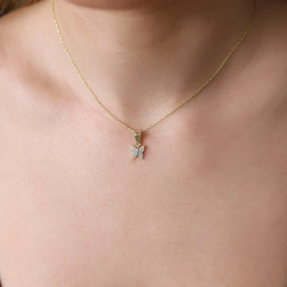 A person wearing a gold-colored necklace with a butterfly pendant.