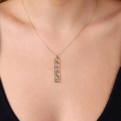 A close-up image of a person wearing a gold-colored Egypt cartouche necklace with a hieroglyph pendant.