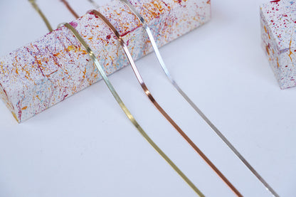 Two gold bangles on a white surface with colorful packaging in the background