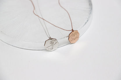 Two engraved pendant necklaces on a clear surface, one with a silver finish and the other with a rose gold finish.