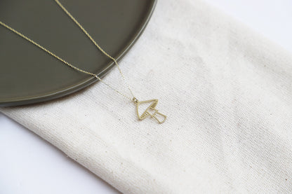 A close-up image of a person's hand holding a dainty gold necklace with a mushroom pendant.