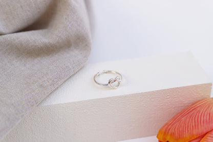 Silver ring on a white surface with a beige fabric and orange flower petal in the background