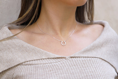A woman wearing a silver horseshoe necklace on a delicate chain, displayed against a neutral background.