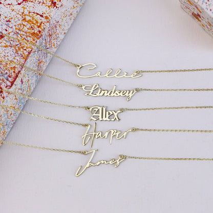A close-up image of some gold-filled nameplate necklaces with the name written in a different cursive fonts on a chain.