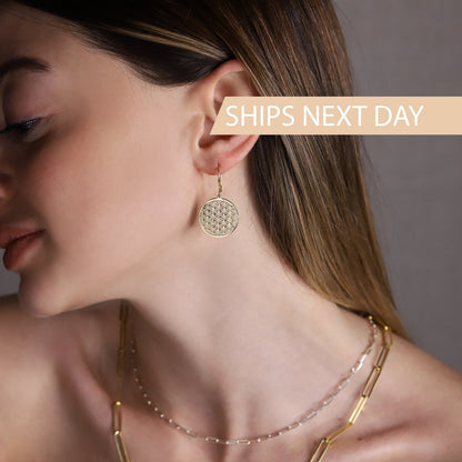 A women wearing a gold earrings featuring the Flower of Life pattern.