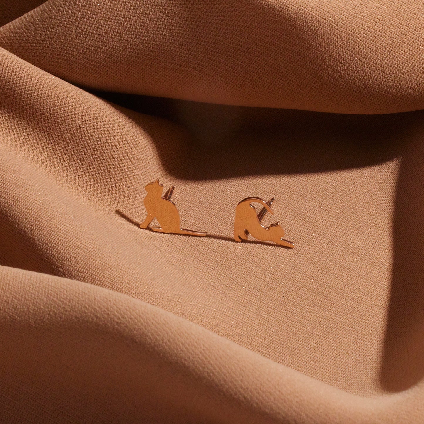 Pair of cat-shaped earrings on a beige fabric background