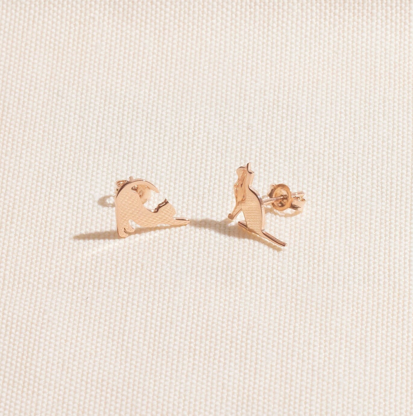 Rose gold bear-shaped earrings on a light beige fabric background