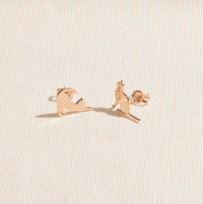 Rose gold bear-shaped earrings on a light beige fabric background