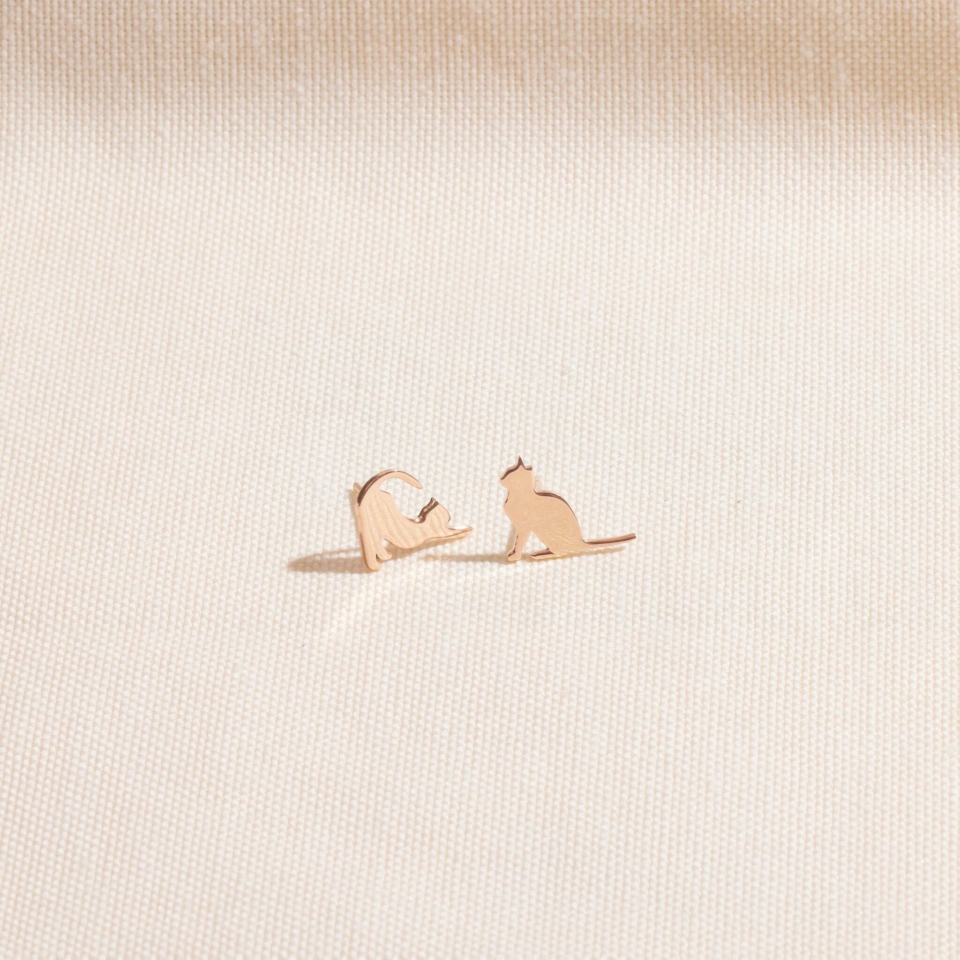 Rose gold cat-shaped earrings on a light beige textured background
