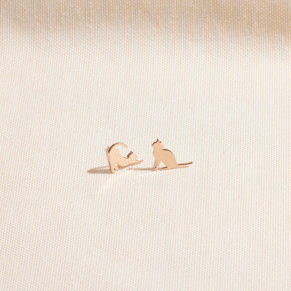 Rose gold cat-shaped earrings on a light beige textured background