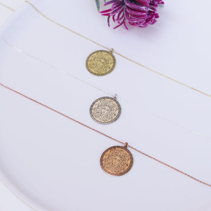 A close-up image of a person's fingers holding a silver necklace with a circular pendant featuring a design.
