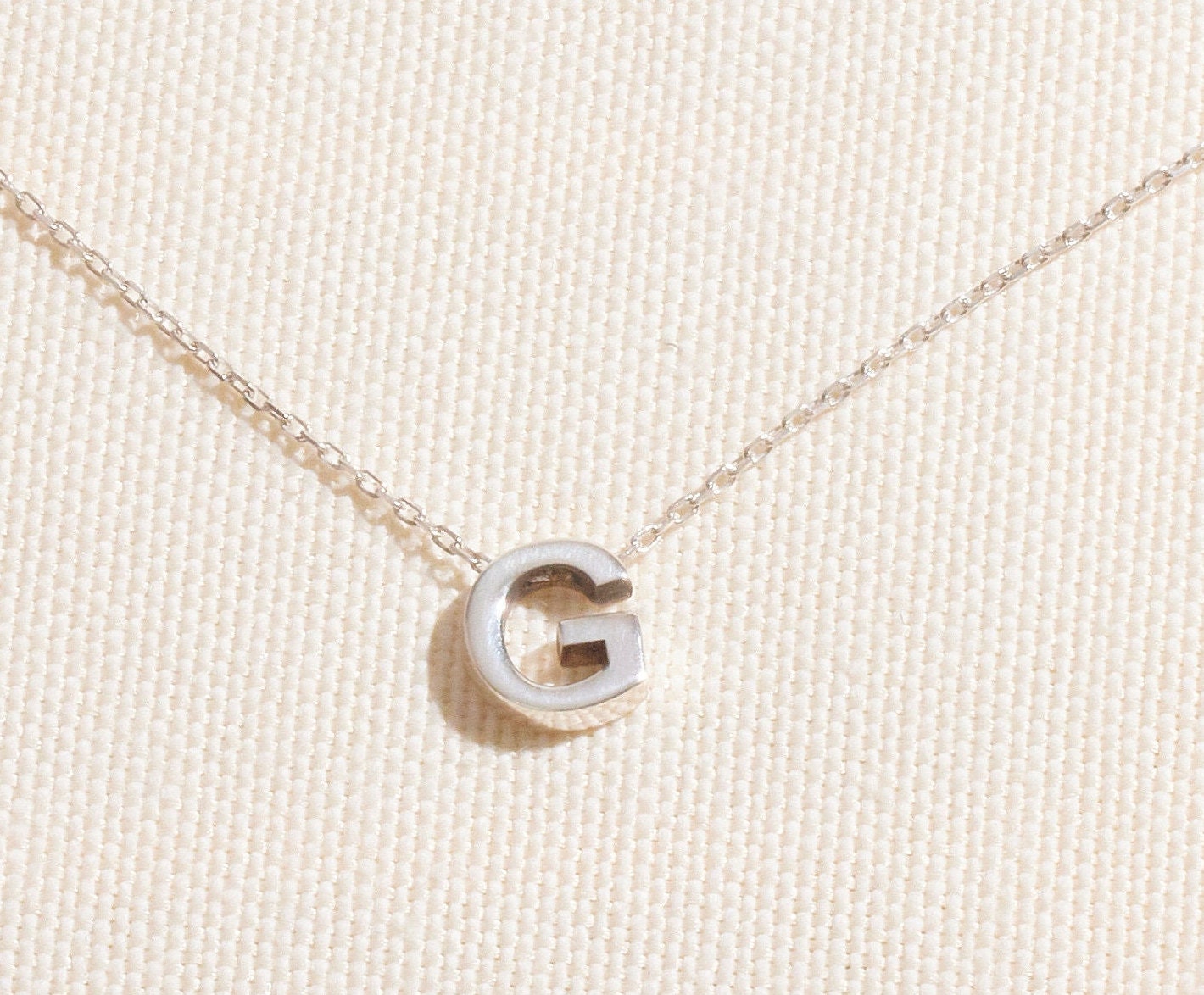 Silver necklace with a 'G' pendant on a beige background