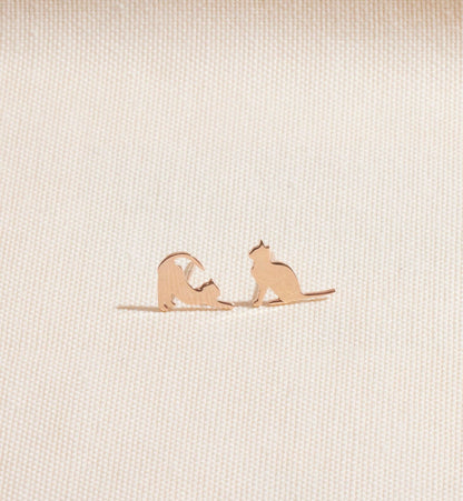Rose gold cat-shaped earrings on a beige fabric background
